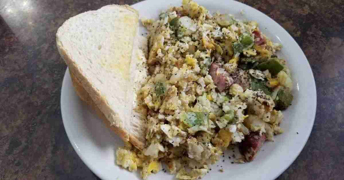 A plate of scrambled eggs, vegetables, sausage, and toast from Depot