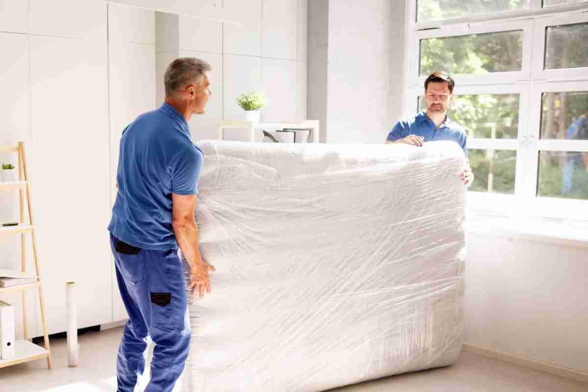 Two Hide-A-Way-Hills movers in blue polo shirts carrying a mattress