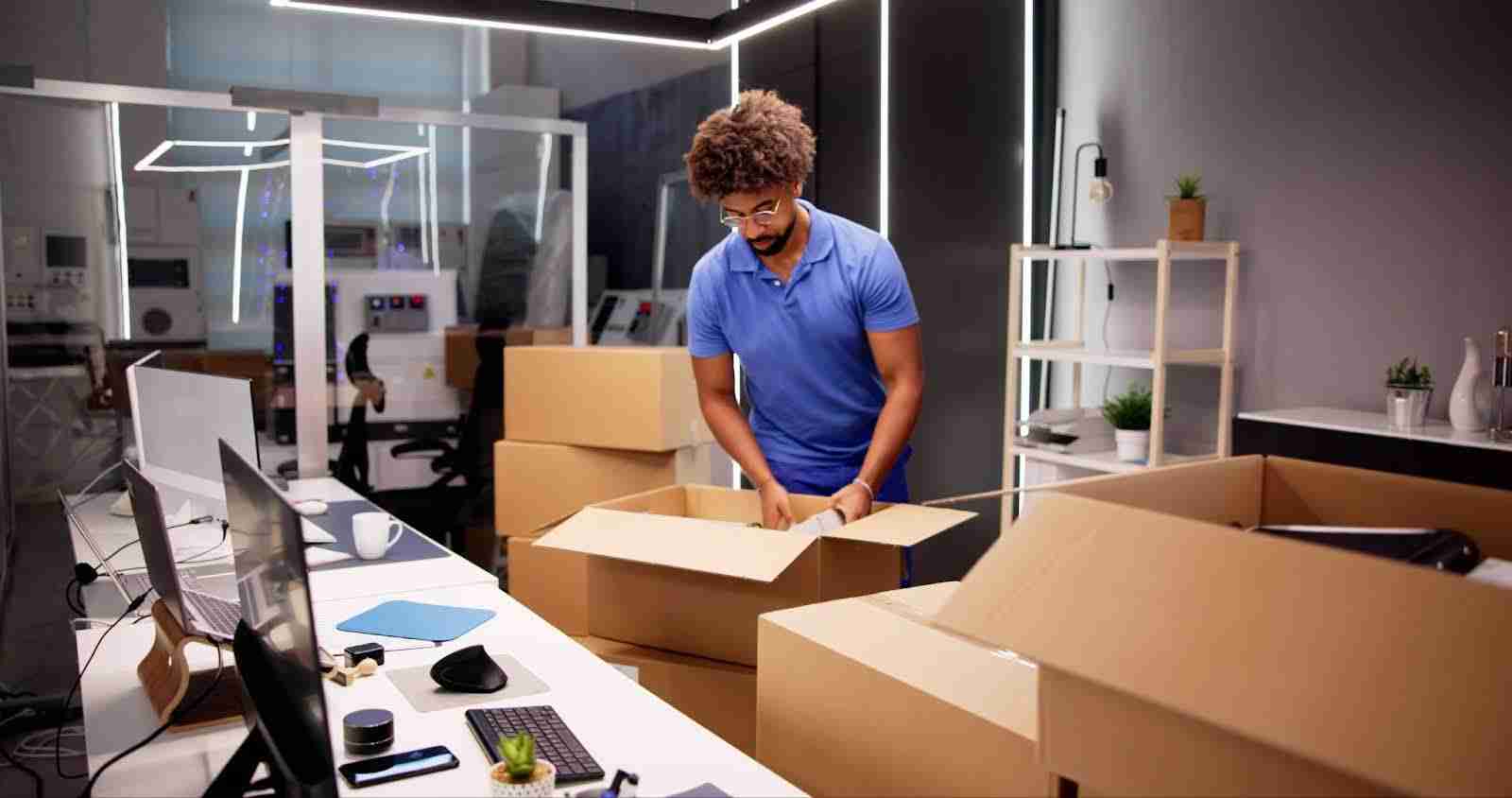 Man in blue polo packing up boxes in his office.
