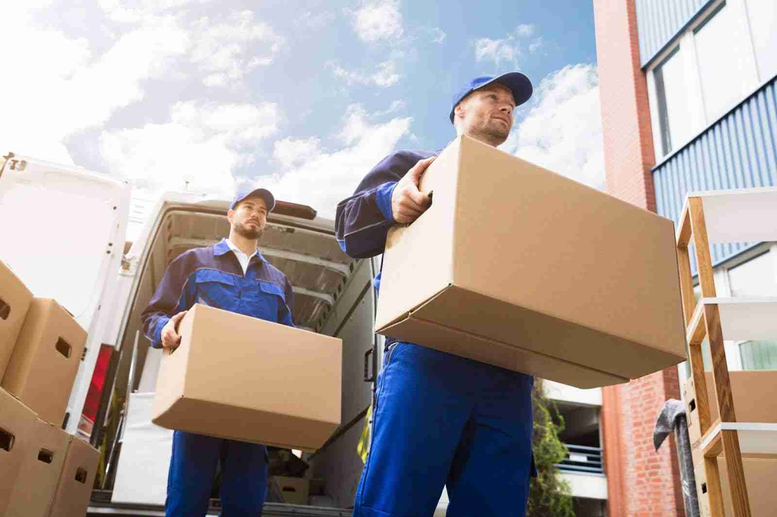 two movers in dressed in blue carrying boxes out of a moving van